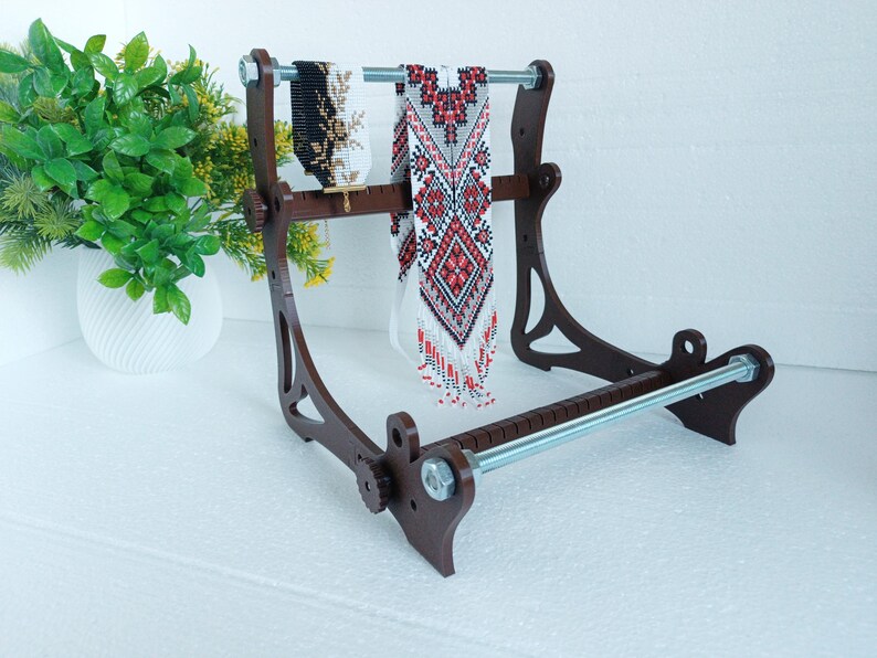 May include: A wooden stand with two beaded necklaces hanging from it. The stand has a metal rod across the top and a metal rod across the bottom. The stand is brown and the necklaces are white and red.