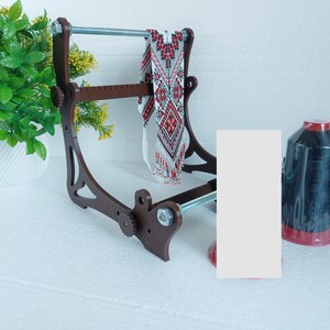 May include: A wooden bead loom with a red and white beaded necklace on it. A spool of black thread is on the right side of the image.
