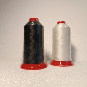 May include: Two spools of thread, one black and one white, with red plastic caps. The spools are wrapped in clear plastic.