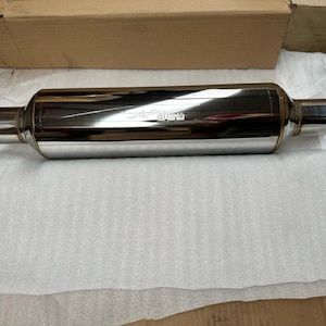 May include: A shiny silver exhaust muffler with a round shape and two ends. The muffler has the text "Flowmaster" printed on it.