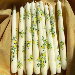 May include: A bunch of white taper candles with a lemon and leaf design painted on them.