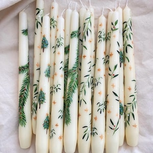 Könnte beinhalten: Elfenbeinfarbene Spitzkerzen mit handgemalten grünen Blättern, Weihnachtsbäumen und goldenen Sternen. Diese dekorativen Kerzen sind perfekt für die Weihnachtsdekoration. Jede Kerze ist etwa 25 cm hoch.