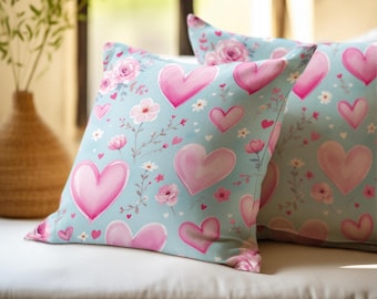 May include: Two light blue throw pillows with a pink watercolour heart and floral pattern.