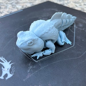 May include: A light gray 3D printed figurine of a creature with a long tail and a textured surface.
