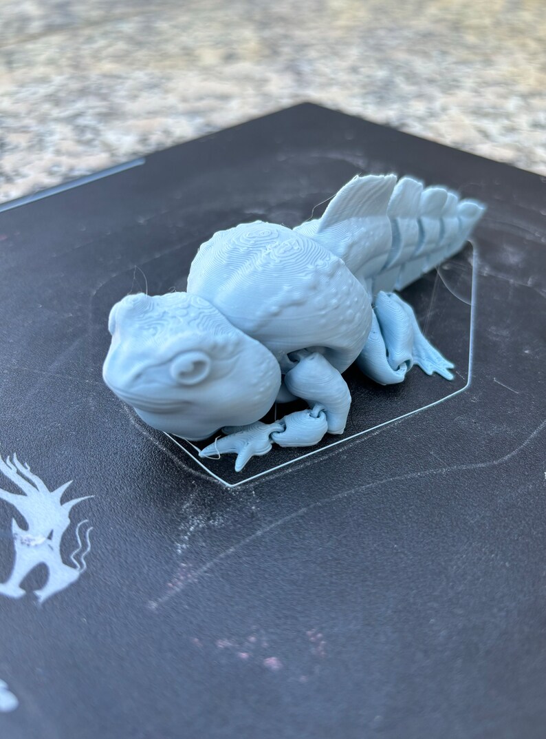 May include: A light gray 3D printed figurine of a creature with a long tail and a textured surface.