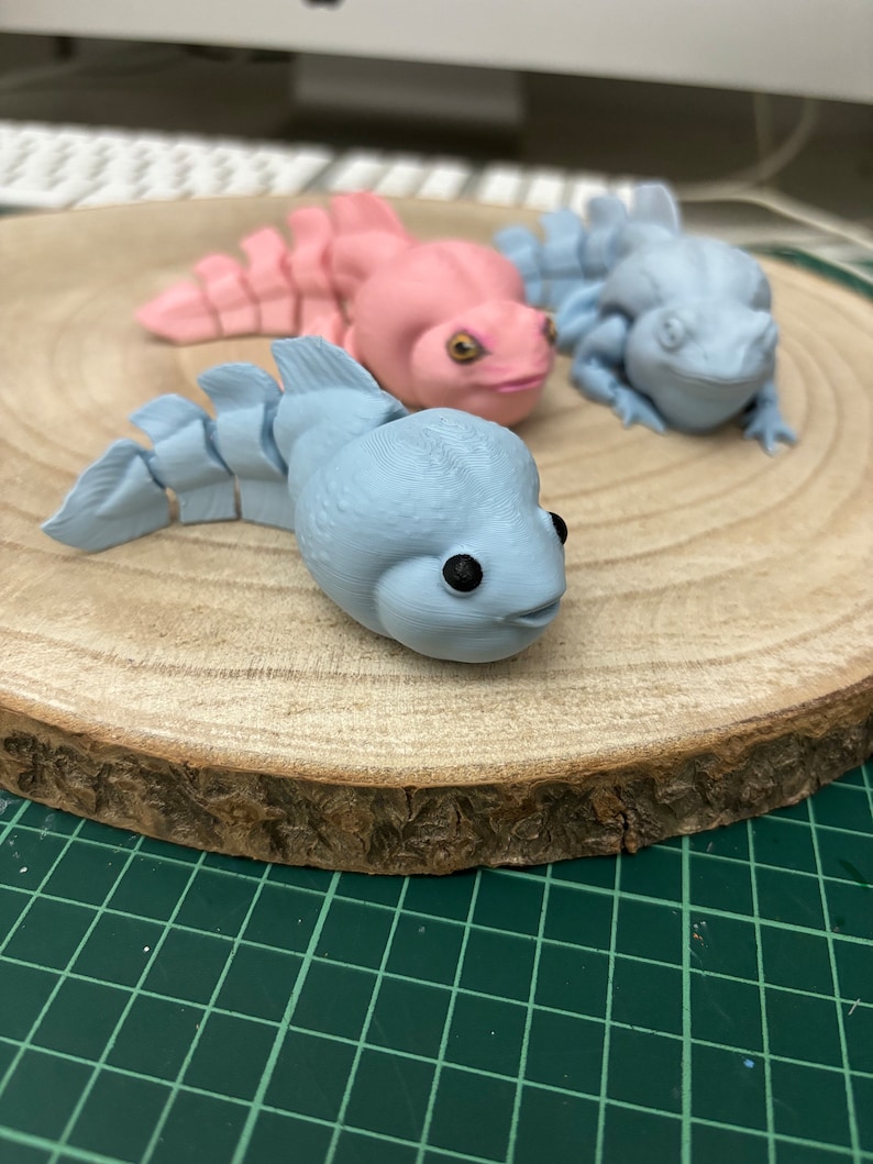 May include: Three small, hand-painted figurines of aquatic creatures on a wooden base. The figurines are painted in shades of blue and pink. The base is made of natural wood with a rough texture.