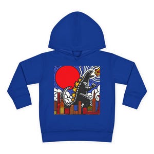 May include: Royal blue hoodie with a graphic of a Godzilla-like monster breathing fire over a city skyline. The graphic includes a red sun and stylized clouds. The hoodie has long sleeves and a hood.