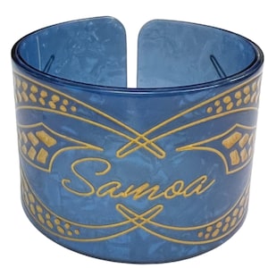 May include: A blue plastic bracelet with a gold design and the word "Samoa" written in cursive.
