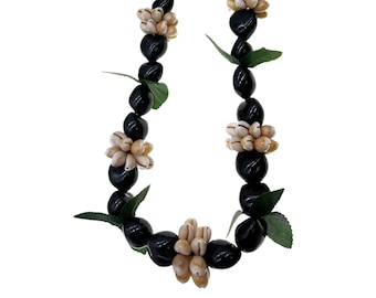 Puede incluir: Un collar de flores de concha blanca, hecho con cuentas negras y hojas verdes. Las flores de concha están dispuestas en un racimo de cinco.