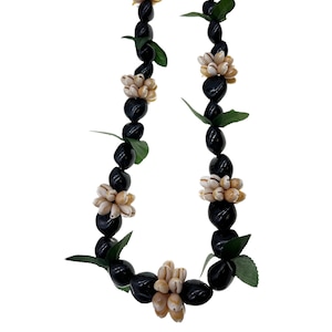 May include: A black and green lei with white shell flowers. The lei is made of black beads and green leaves. The shell flowers are arranged in a cluster of five.