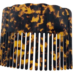 Puede incluir: Un peine de carey con una parte superior ondulada y una fila de dientes. El peine está hecho de un material plástico marrón y amarillo.