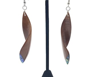 Puede incluir: Un par de pendientes de madera marrón con un diseño retorcido. Los pendientes tienen un pequeño detalle de concha de abulón iridiscente en la parte inferior.