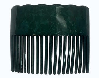 Puede incluir: Un peine para el cabello de color verde bosque oscuro con un patrón moteado y jaspeado en todo el cuerpo. El borde superior tiene un diseño ondulado y festoneado, mientras que la parte inferior consta de catorce dientes largos y rectos.