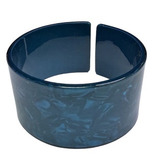 May include: A wide blue plastic bangle bracelet with a marbled pattern. The bracelet is open on one side and has a glossy finish.
