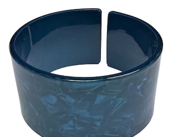 Puede incluir: Un brazalete ancho de plástico azul con un patrón de mármol. El brazalete está abierto por un lado y tiene un acabado brillante.