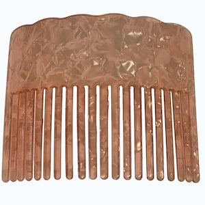 Puede incluir: Un peine para el cabello de color melocotón con un borde superior ondulado y una serie de dientes verticales. El peine tiene un aspecto veteado y texturizado, y está hecho de un material translúcido.