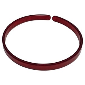 May include: A red open cuff bracelet. The bracelet is a solid, deep red color and has a smooth, polished surface. The design is a simple, elegant circle that does not fully close, leaving a small gap.