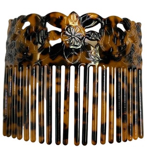May include: A brown and black tortoiseshell hair comb with a decorative floral design. The comb has a wide, curved top and a row of teeth along the bottom.