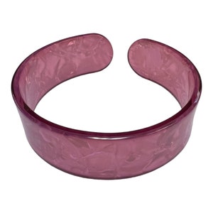 May include: A wide, pink plastic bangle bracelet with a marbled effect.