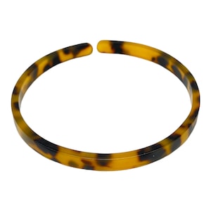 Puede incluir: Un brazalete de color marrón y amarillo con estampado de caparazón de tortuga.
