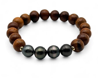 Puede incluir: Un brazalete de cuentas de madera marrón con cuatro perlas negras. El brazalete tiene detalles dorados.