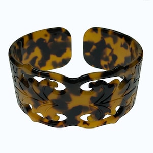 Può includere: Un braccialetto rigido in tartaruga marrone e nero con un design floreale intagliato.