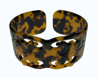 May include: A brown and black tortoiseshell bangle bracelet with a carved floral design.