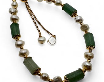 May include: A gold-toned adjustable bracelet featuring alternating green cylindrical beads and irregular white pearls. The bracelet has a delicate chain with two pearl-like charms and a small, clear, round charm.