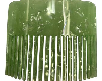 Puede incluir: Un peine ancho para el cabello con un color base verde claro y un patrón blanco translúcido moteado en todo el material. El borde superior del peine tiene un diseño festoneado, mientras que la parte inferior consta de catorce dientes rectos.