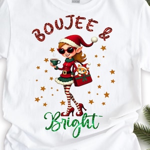 Può includere: T-shirt bianca con grafica a tema natalizio. Il design presenta un personaggio simile a un elfo con un abito rosso e occhiali da sole, che tiene in mano una tazza di caffè. Il testo "Boujee & Bright" è scritto in rosso e verde glitterato.