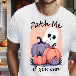 以下が含まれることがあります： ハロウィーンをテーマにしたグラフィックがプリントされた白いTシャツ。デザインは、お化け、紫とオレンジ色のカボチャ、そして「Patch Me if you can」というテキストが特徴です。Tシャツは人が着ています。