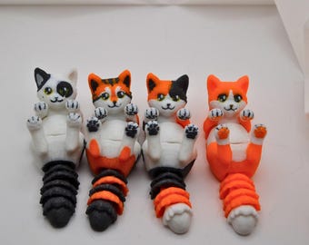 May include: Four whimsical cat-shaped figurines. Each cat is lying on its back with paws up, featuring a white belly and a colorful head and tail. The tails are black and orange, and the cats' heads are white, orange, and black.