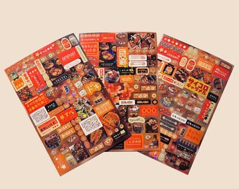 May include: Three sheets of stickers featuring Japanese food illustrations and text. The stickers are printed on a gold background with red and black accents. The text includes "サイコロ キャラメル" and "ドギ".