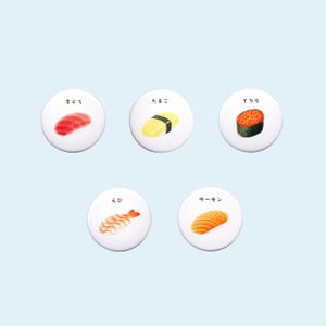 Może przedstawiać: Pięć białych, okrągłych guzików z japońskim tekstem i obrazkami różnych rodzajów sushi. Guziki przedstawiają obrazy tuńczyka, jajka, łososia, krewetek i ikury.