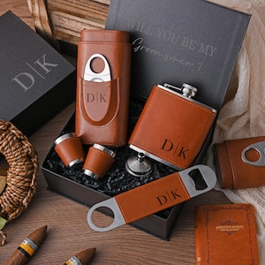 May include: A brown leather gift set with a flask, cigar cutter, shot glasses, and bottle opener. The set includes a box with the text "WILL YOU BE MY Groomsmen?" and the initials "DK".