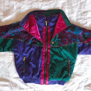May include: A vintage jacket in a vibrant color block design. The jacket features a combination of purple, teal, and green panels, with a pink center stripe and collar. The collar and shoulders have a quilted pattern, and the jacket has a gold zipper.