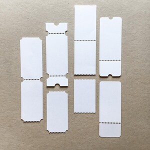 Op de afbeelding: Een verzameling van zes blanco witte papieren tickets, verticaal gerangschikt. Elk ticket heeft geperforeerde randen, sommige met afgeronde uitsparingen aan de uiteinden en andere met rechte gekartelde randen, gemaakt van wit karton.