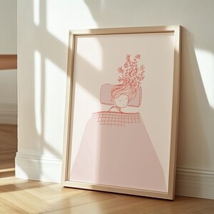 Könnte beinhalten: Ein gerahmter Kunstdruck mit einer Strichzeichnung einer schlafenden Person im Bett. Das Haar der Person ist mit floralen Elementen geschmückt. Das Kunstwerk ist hauptsächlich in Rosa- und Rottönen gehalten, mit einem hellbeigen Hintergrund und einem Holzrahmen.