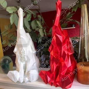 May include: Two geometric sculptures, one white and one red, sit side-by-side. The white sculpture has the Greek letters Delta, Sigma, and Theta. The red sculpture has the Greek letter Delta and a square. Both have a faceted design.