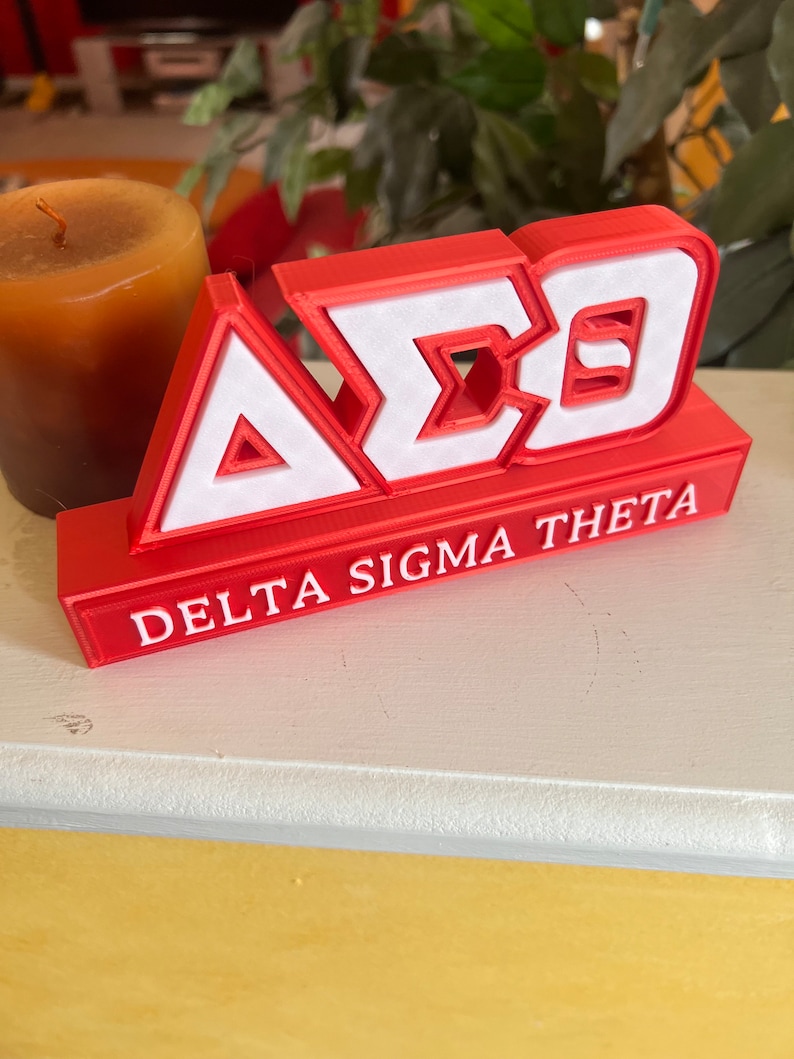 Może przedstawiać: Czerwony blok wydrukowany w 3D z literami "A&Sigma;&Theta;" w kolorze białym i słowami "Delta Sigma Theta" w kolorze białym pod literami.