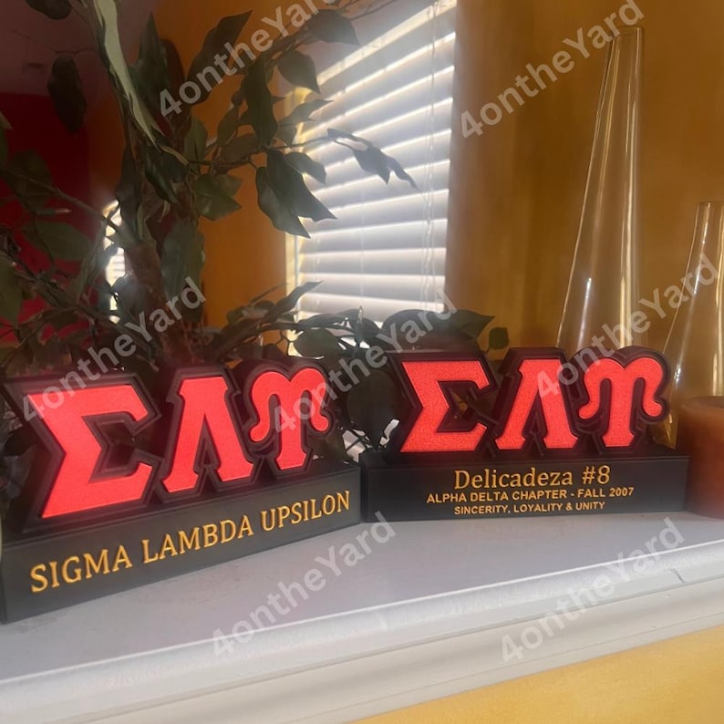 May include: Two illuminated red and black Sigma Lambda Upsilon fraternity signs. One sign reads "Sigma Lambda Upsilon" in gold lettering. The other sign reads "Delicadeza #8" with "Alpha Delta Chapter - Fall 2007" and "Sincerity, Loyalty & Unity".