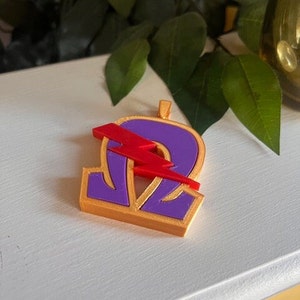 May include: A purple and gold pendant with a red lightning bolt design. The pendant is shaped like the Greek letter Omega.