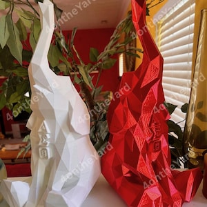 May include: Two geometric elephant sculptures, one white and one red, are displayed side-by-side. The white elephant has the Greek letters Alpha, Sigma, and Omega, and a square symbol. The red elephant has the letter E. Both are on a white surface.