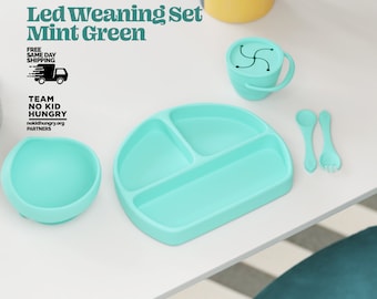 May include: A mint green silicone weaning set with a divided plate, bowl, spoon, and fork. The set is designed for babies and toddlers learning to eat solid foods.