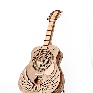Puede incluir: Reloj de madera con forma de guitarra con intrincados detalles cortados con láser. El reloj presenta una esfera con engranajes, alas y las palabras "ROCK N ROLL" y "TIME HUNTER". La guitarra es de madera marrón claro.