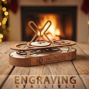 Può includere: Una scultura cinetica in legno con un complesso sistema di ingranaggi e una parte superiore decorativa. La base presenta il testo "TIME HUNTER" e "ENGRAVING AVAILABLE". La scultura è posta su una superficie di legno con uno sfondo sfocato.