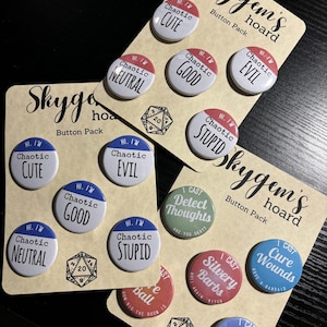 May include: A set of 10 round, colorful buttons with various text and images. The buttons are arranged in two rows of five. The top row features buttons with the text "HI. I'M Chaotic" followed by "CUTE", "GOOD", "EVIL", and "STUPID". The bottom row features buttons with the text "I CAST" followed by "Detect Thoughts", "Silvery Barbs", "Cure Wounds", and "Misty Step".