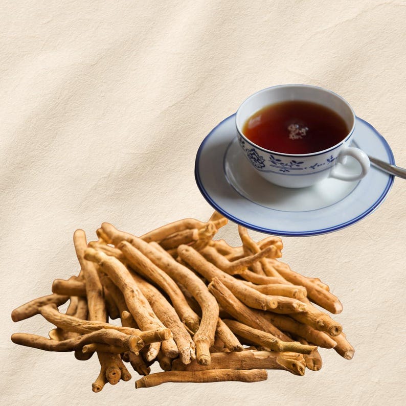 Puede incluir: Una taza de t&eacute; sobre un platillo con un dise&ntilde;o floral azul, y un mont&oacute;n de ra&iacute;ces secas de color marr&oacute;n claro. El t&eacute; es de color marr&oacute;n oscuro. El fondo es de color beige claro.