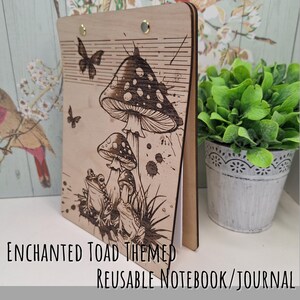 May include: A wooden notebook with a whimsical design featuring a toad, mushrooms, and butterflies. The notebook is titled "Enchanted Toad Themed Reusable Notebook/Journal".