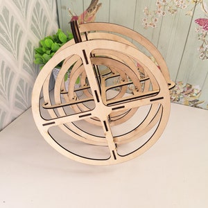 May include: A wooden, circular, multi-tiered stand with a natural wood finish. The stand is made of several concentric circles that are stacked on top of each other.